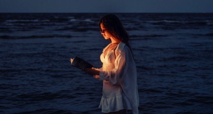 a fair skinned nwoman reading a book being illuminated with a light while standing in the sea.jpg.optimal