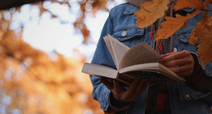 person holding book in fall leaves.jpg.optimal