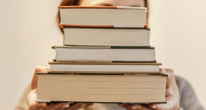 fair skinned person holding a stack of books.jpg.optimal